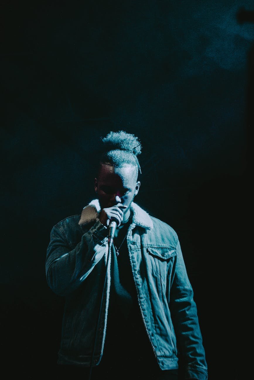 man wearing denim jacket singing on stage