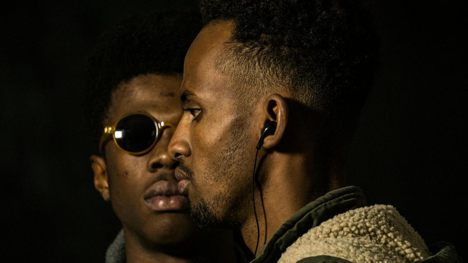 man wearing earphones near man in sunglasses